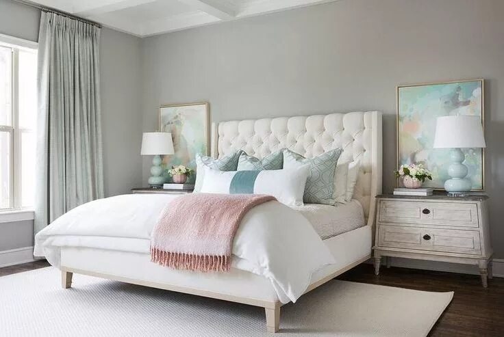 Пастельный интерьер спальни A cream tufted headboard with white bedding and blue pillows provides a serene c