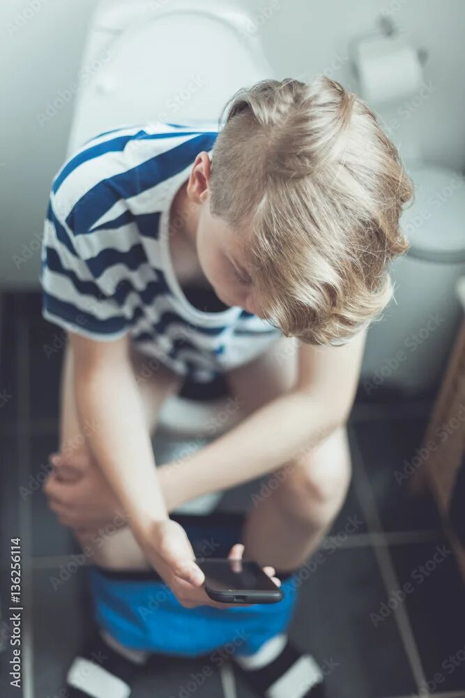 Подростки в туалете фото Teenage boy sitting on a toilet with his mobile фотография Stock Adobe Stock