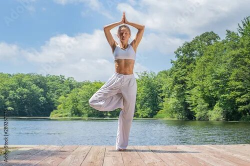 Поза дерева в йоге фото Attractive woman is practicing yoga, doing Vrksasana exercise, standing in tree 