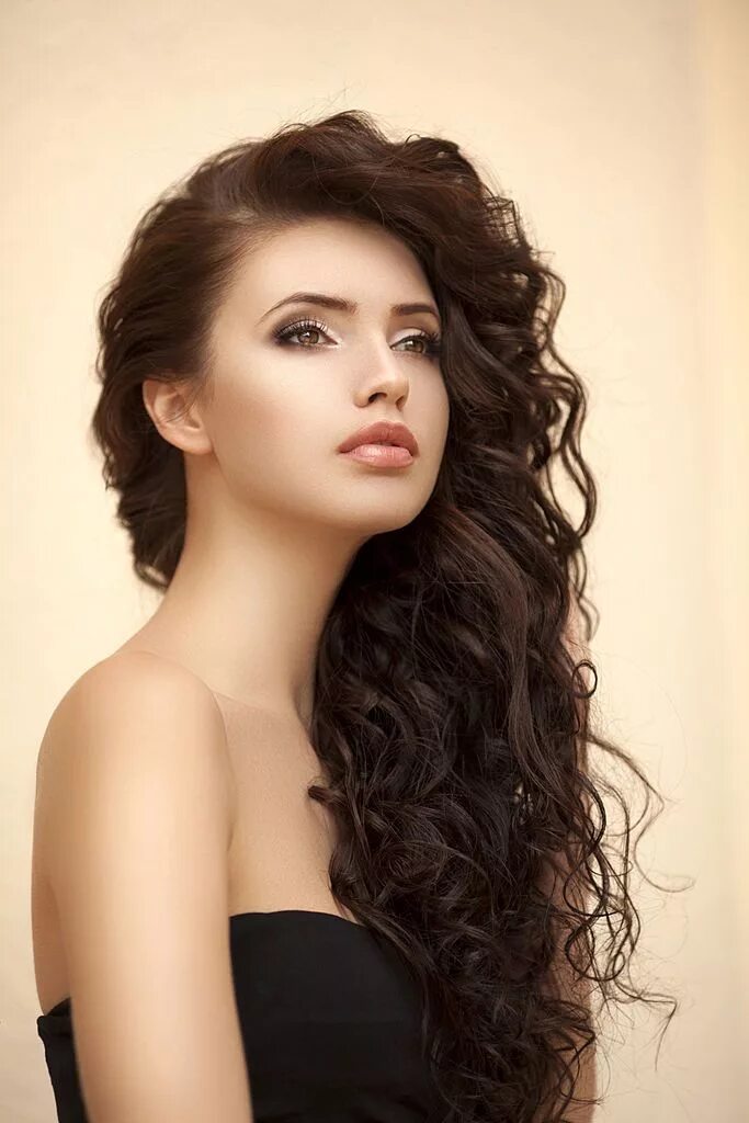 Прическа на длинные волнистые волосы Outdoor shot of young beautiful woman on light background.... Long curly haircut