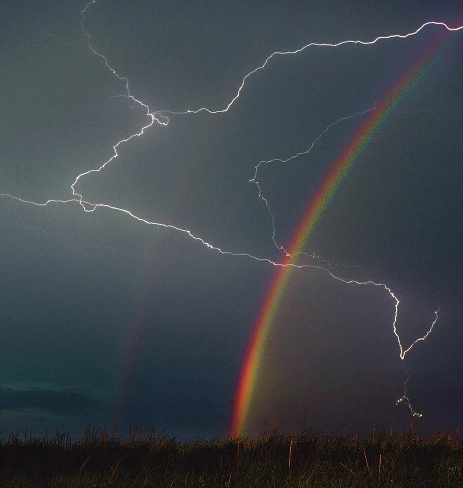 Природные явления фото A lightning strike passes through a rainbow that appeared over the sand dunes on