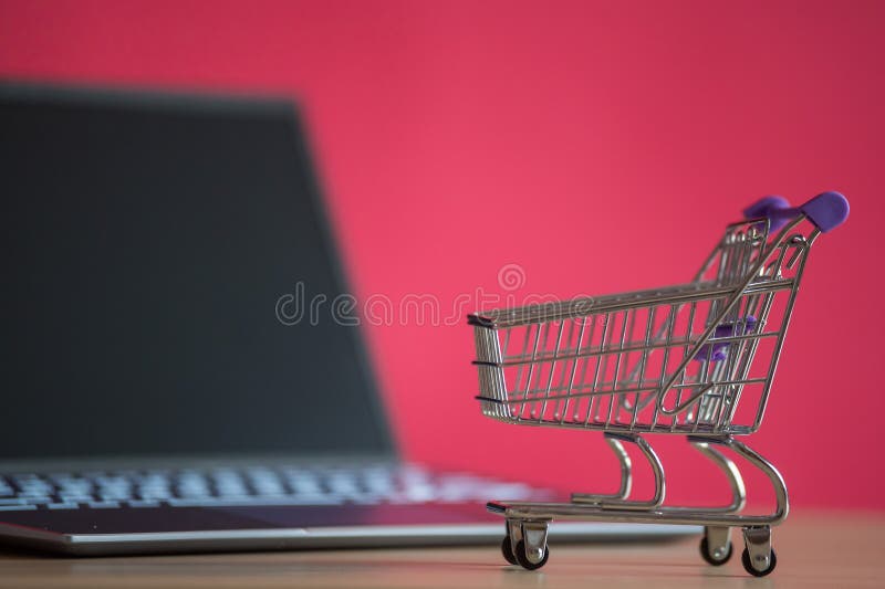 Про фото интернет магазин Online Shopping Concept. Mini Grocery Cart and Laptop on a Pink Background. Smal