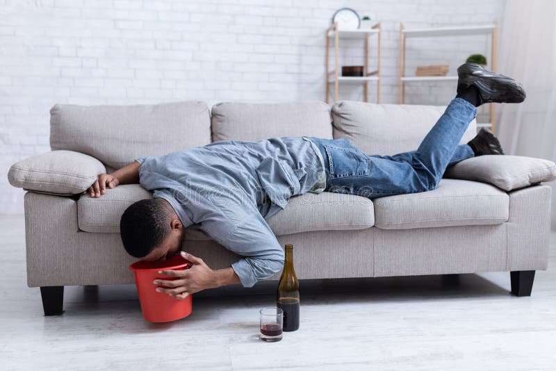 Пьяный на диване фото Drunk Man Vomiting into Bucket after Drinking Wine Lying Indoor Stock Image - Im