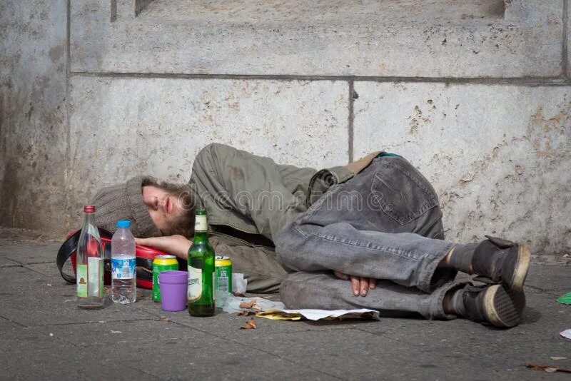 Пьяный на улице фото Homeless Young Alcohol Addict Lying Drunk on Street Sidewalk in Berlin. Editoria