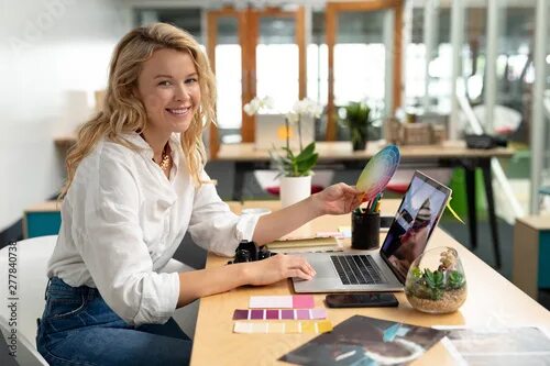 Работа дизайнера интерьера удаленно без опыта Female graphic designer holding a color swatch while using laptop at desk in off