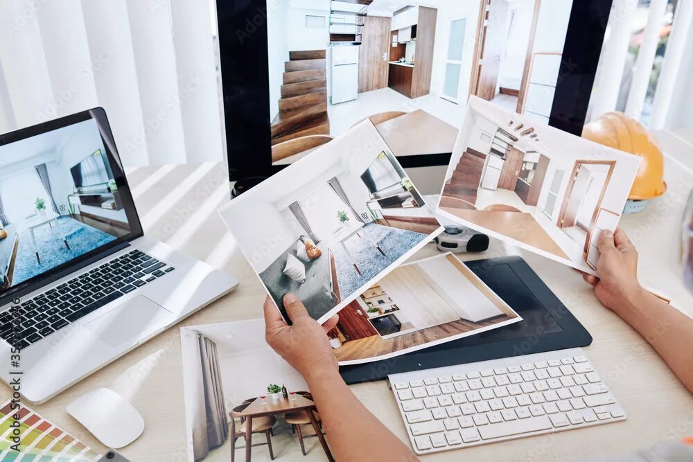 Работа дизайнером интерьера удаленно Interior designer sitting at desk and looking at printed photos of clients rooms