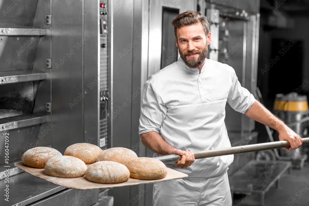 Работа над фото Handsome baker in uniform taking out with shovel freshly baked buckweat bread fr