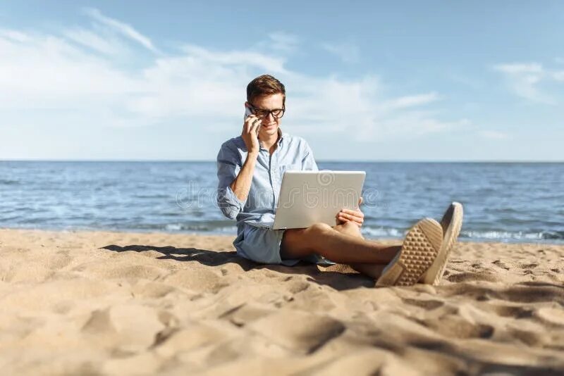 Работа в море фото Young Guy with Glasses, Working on His Laptop and Talking on the Phone on the Be