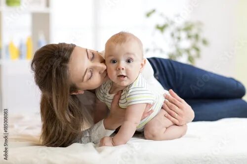 Ребенок будет маму фото Mom kissing her little son on bed. Mother embracing infant baby. - Buy this stoc